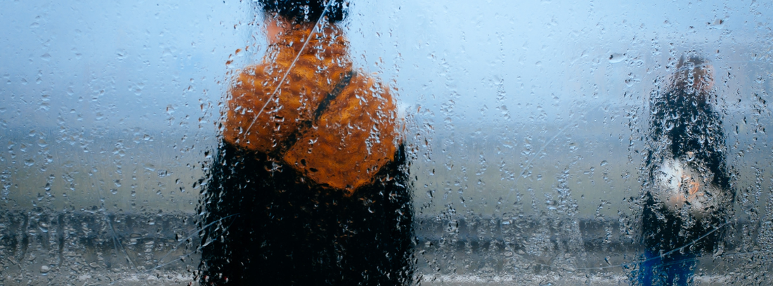 two people standing in the rain viewed through a wet and foggy window